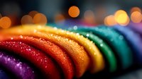 Vibrant rainbow colored macarons in a row with water droplets and bokeh background, showcasing delicate texture and gradient colors from red to purple.