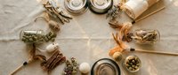 Rustic autumn wreath made from natural materials including pinecones, cinnamon sticks, dried herbs and candles arranged on neutral linen background.