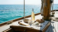 Bottle of wine with bread and cheese on wooden table aboard sailing boat on turquoise sea, nautical dining experience for travel and lifestyle content.