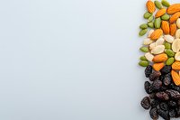 Mixed nuts and dried fruits arranged on right border of white background, including almonds, pistachios and raisins, creating minimalist composition for healthy snacking.