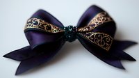 Elegant dark purple satin bow with ornate golden lace trim and emerald center detail on isolated background, suitable for fashion and craft projects.