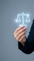 Hand holding glowing neon scales of justice symbol against gray background. Legal professional displaying digital law, compliance, and fairness concept for business and corporate use.