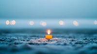 Single glowing candle on sandy beach at dusk with blurred bokeh lights in background creates peaceful atmospheric scene for meditation and spiritual concepts.