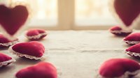 Romantic red rose petals scattered on rustic wooden surface with soft window light creating warm atmosphere for Valentine's Day celebration and love themes.