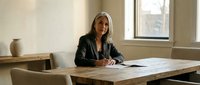 Professional blonde businesswoman working at wooden desk in modern office space with natural lighting and minimalist decor for corporate presentations.