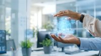 Professional hands holding glowing digital hologram with data cubes in modern office environment, representing technology innovation and business solutions.