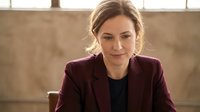 Confident Caucasian businesswoman in burgundy blazer sitting at desk, thoughtful expression, soft natural light, professional office setting.