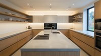 Modern minimalist kitchen interior with wooden cabinets, white countertops, built-in appliances and recessed lighting for contemporary home design.