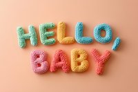 Colorful crocheted letters spelling HELLO BABY on soft pink background for nursery decor and baby shower celebrations.