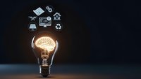 Glowing light bulb with brain filament and floating technology icons representing innovation, creativity and smart solutions on dark background.