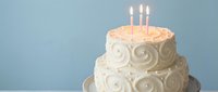 Elegant two-tier white birthday cake with decorative swirl frosting and three lit candles on blue background for celebration events and party planning.
