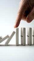 Hand stopping domino effect with finger preventing chain reaction of falling white blocks on clean background for business crisis management concepts.