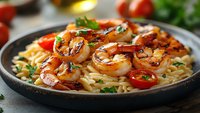 Grilled shrimp with pasta and cherry tomatoes garnished with fresh herbs in cast iron skillet, ready for restaurant menu or cooking blog content.