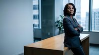 Confident African American businesswoman in suit standing by office desk with arms crossed, city skyline view through windows for corporate leadership.