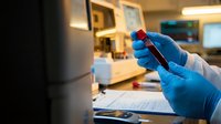 Medical laboratory technician in blue gloves holding blood sample tube for testing and analysis in modern clinical research facility.