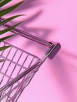 Shopping cart handle and palm leaf shadow on pink background, minimalist retail concept with creative lighting and modern composition for commercial design.