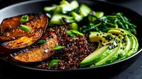 Nutritious quinoa bowl with roasted sweet potato, sliced avocado and fresh herbs in black plate. Healthy vegan meal for balanced diet and wellness lifestyle.