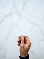 Hand holding blank white card against marble background, ideal for business cards, invitations, and promotional designs.