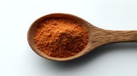 Ground red chili powder in wooden spoon on white background, macro food photography showing texture and color of spicy seasoning ingredient.