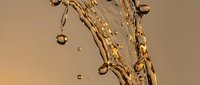 Golden liquid splashing dynamically with droplets suspended in mid-air against warm beige background. Suitable for beverage, cosmetics, and luxury product advertising.