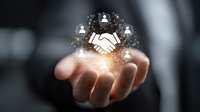 Business professional holding glowing digital handshake icon with network connections, representing partnership, collaboration and business agreement in corporate environment.