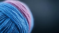 Close-up macro shot of pink and blue yarn balls showing detailed twisted fiber texture against dark background, selective focus creates dreamy crafting atmosphere.