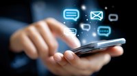 Hand holding smartphone with glowing message icons floating above screen, depicting digital communication and mobile messaging on dark background.