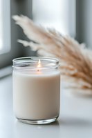 Lit white scented candle in glass jar with pampas grass decoration on windowsill, creating cozy atmosphere for relaxation and mindfulness practice.