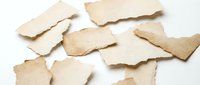 Torn aged paper pieces with rough edges scattered on white background for vintage design projects and creative artwork applications.