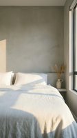 Serene bedroom corner with unmade bed, white linens, textured sage green wall, natural sunlight, minimalist decor, and dried pampas grass in ceramic vase for interior design.