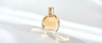 Elegant golden perfume bottle with round glass design and metallic cap casting soft shadows on white surface for fragrance branding.