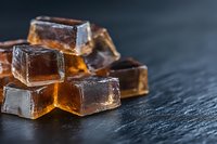 Amber-colored sugar candy cubes with condensation drops stacked on dark slate background, macro shot highlighting transparency and crystalline structure.