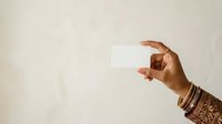Hand holding blank white business card against neutral beige background, suitable for branding, corporate identity, and marketing mockup presentations.