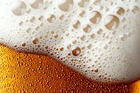 Fresh cold beer with bubbles and foam close up macro shot, golden amber liquid with condensation droplets and white frothy head. Perfect for bar menu design.
