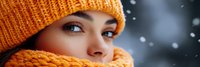 Young woman with brown eyes wearing orange knit hat and scarf in winter snowfall. Cozy seasonal fashion portrait for cold weather clothing advertisements.