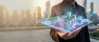 Businessman holding holographic city model with digital buildings and urban infrastructure projection in hands against blurred skyline background for technology and development concepts.