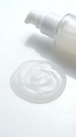 White cosmetic pump bottle dispensing creamy lotion or skincare product onto white surface, isolated on white background for beauty and wellness packaging design.