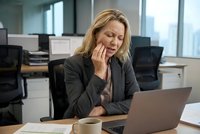 Stressed blonde businesswoman experiencing headache while working on laptop in modern office environment. Professional woman dealing with workplace pressure.