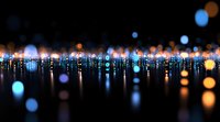Glowing blue and orange bokeh lights reflected on dark glossy surface creating magical nighttime atmosphere with blurred circles and light trails.