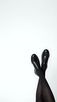 Womens legs in black tights and lace-up oxford shoes raised up against a white background, minimalist fashion concept.