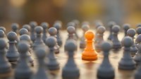 Single orange pawn standing out among gray pawns on wooden board, symbolizing uniqueness, leadership, and competitive advantage in business strategy.