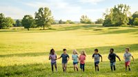 Children running together across green meadow field on sunny day, outdoor activity and summer fun for kids.