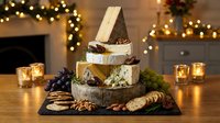 Gourmet cheese platter with crackers nuts and grapes on slate board with warm bokeh lights creating festive holiday atmosphere for entertaining.