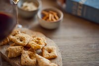 Crispy cheese crackers on wooden board with red wine and snack bowls, perfect for entertaining or gourmet appetizer spread.