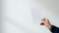 Person holding blank white card or paper against neutral background for mockup, branding, advertising, or presentation purposes.