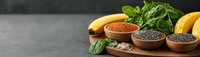 Fresh bananas, citrus fruits and wooden bowls with assorted seeds and chia on dark background with green spinach leaves, panoramic food composition.