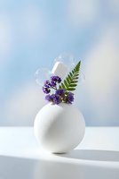 Modern white ceramic vase with purple wildflowers and green fern against soft pastel sky background for home decor and botanical design concepts.