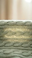 Cozy sage green cable knit sweater texture with intricate braided patterns and soft wool fibers for fashion and textile design projects.