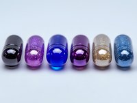 Colorful glass beads with glitter effect arranged in row on white background. Handmade jewelry elements in black, purple, blue, pink, beige and turquoise colors.