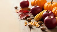 Autumn harvest composition with red apples, orange pumpkins, corn and colorful fall leaves on wooden background for seasonal decorating and thanksgiving.